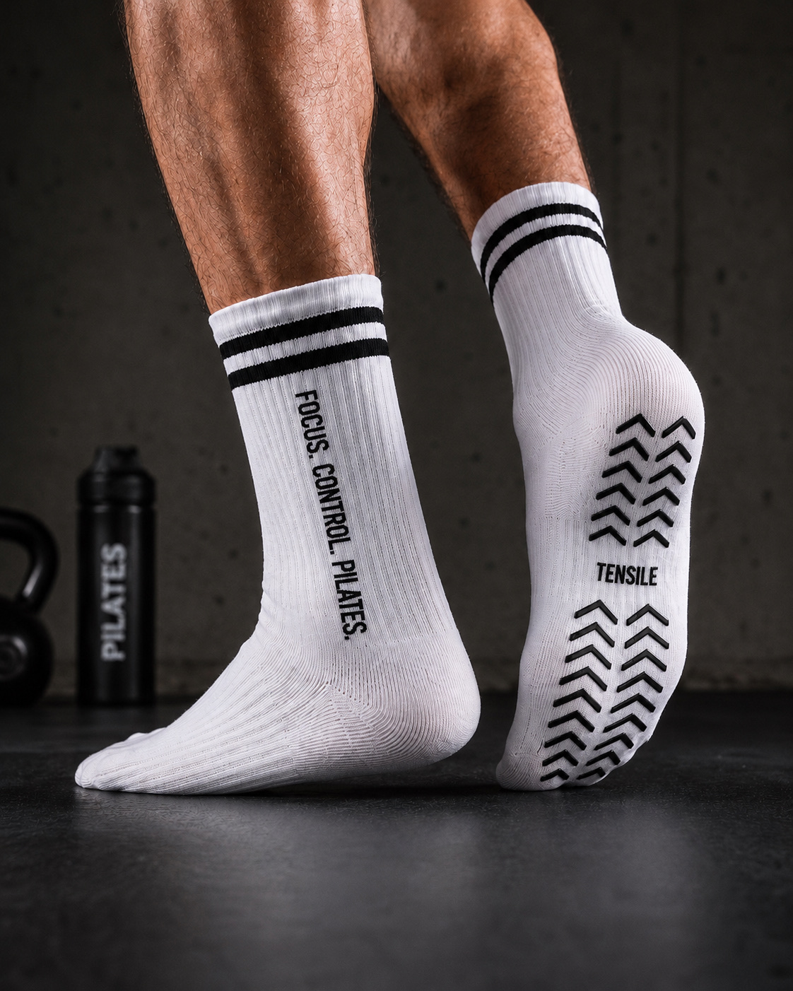 Mann in TENSILE Grip-Socken mit FOCUS. CONTROL. PILATES. Print beim Training auf dunklem Gym-Boden